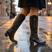Heeled knee high boots for women with pointed toe, mid step on a wet city pavement at dusk