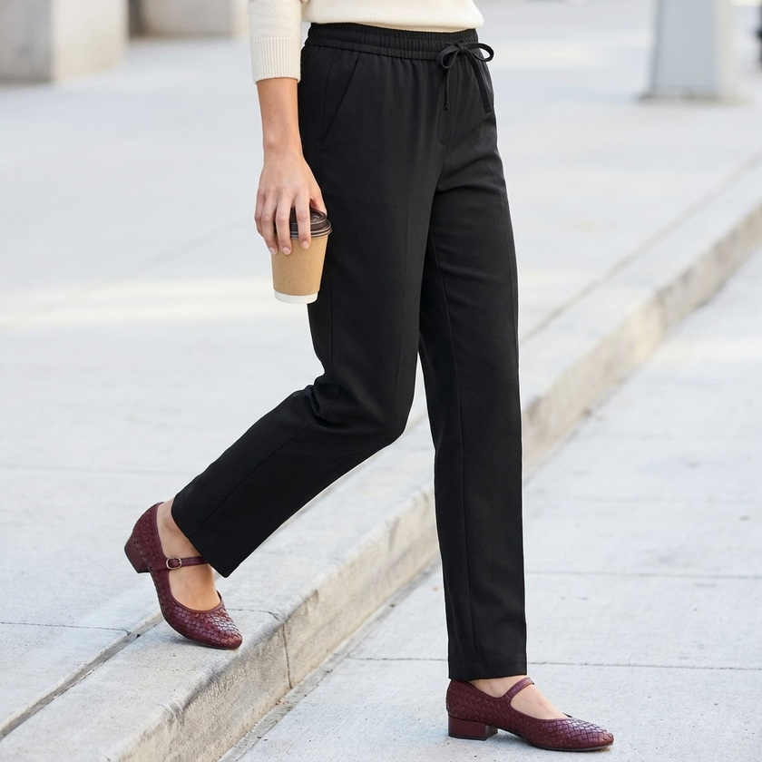 Black pull on straight leg dress pants for women worn with burgundy Mary Jane flats on a sidewalk